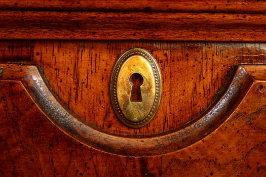 Wooden door of an ancient desk with a decorative metal plate for a key.