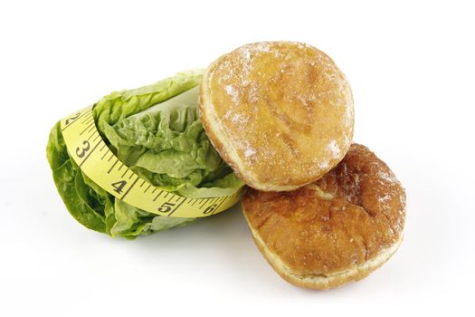 Contradiction between healthy food and junk food using a green salad lettace and jam doughnut with a yellow tape measure on a reflective white background 