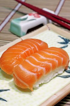 Yummy salmon. A close-up of chopsticks and a square plate with two pieces of salmon nigiri, wasabi and ginger. 