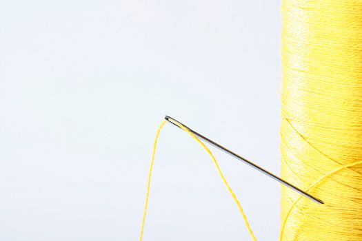 The coil of yellow threads with a needle for sewing.