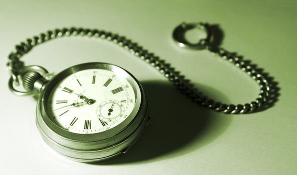 old silver pocket watch; focused on the dial; with a chain, tinted green; gradient background