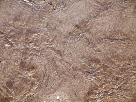 Shallow spring water flowing over sand on a beach in Malta