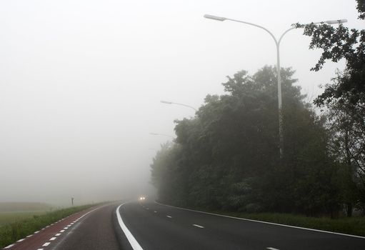  Misty main road with car headlights visible through the mist