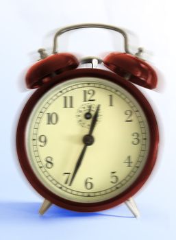 Ringing old style alarm clock (movement blur) - close up on light blue background.