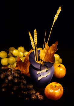 Autumn fruits (grapes and apples) surrounding blue vase; photographed in the dark and on black background.