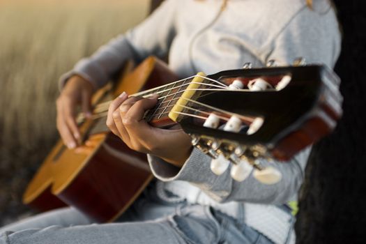 Woman playing her guitar at the sunset (focus is on the left hand) 