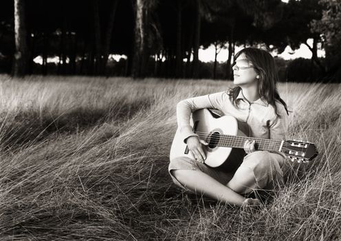 Woman playing her guitar on a meadow at the sunset (toned in PS)
