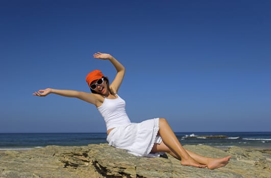 Beautiful happy woman on the beach with a orange hat and white glasses