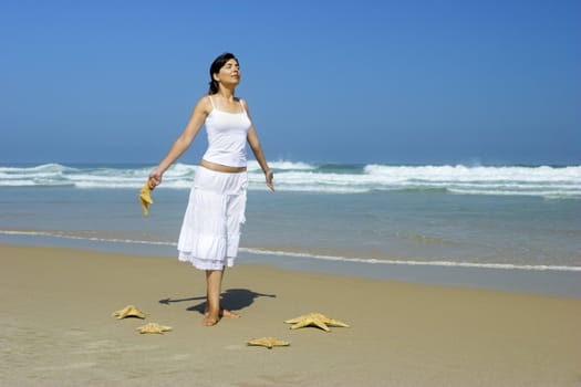 Beautiful woman feeling the breeze with a starfish on the hand and others on the sand