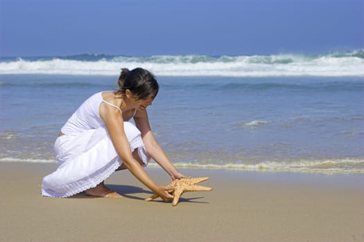 Beautiful woman on the beach puting a starfish on the sand close to the beach