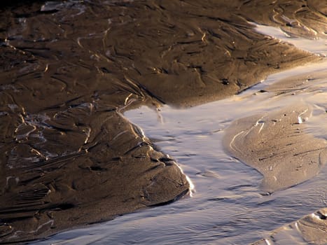 Freshwater spring flowing onto a sandy beach at sunset