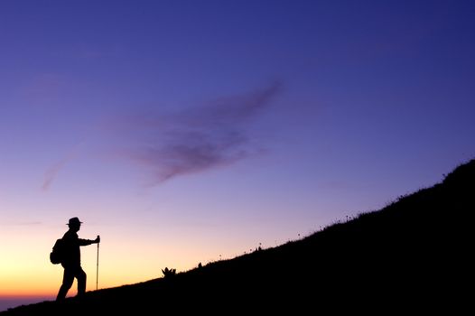 High in the mountains a walker climbs a ridge, silhouetted in the pre-dawn light.