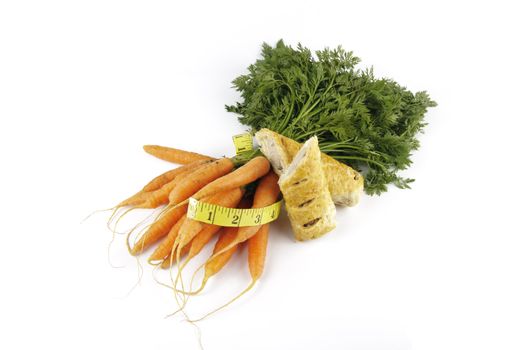 Contradiction between healthy food and junk food using bunch of carrots and sausage roll with a tape measure on a reflective white background 