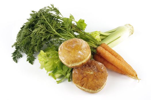 Contradiction between healthy food and junk food using a bunch of carrots and celery with two doughnuts on a reflective white background 