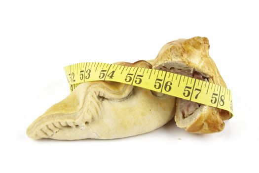 Single golden pasty with pork pie and yellow tape measure on a reflective white background