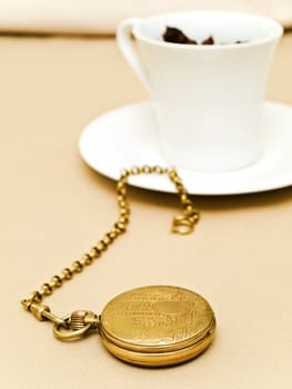  old pocket watch near the cup of tea at beige 