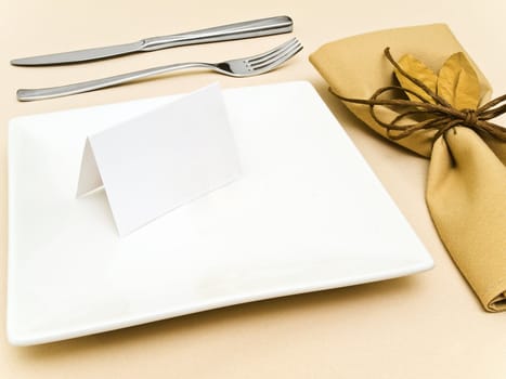 decorated table serving with golden bay leaves in serviette and cord near plate, knife and fork at beige 