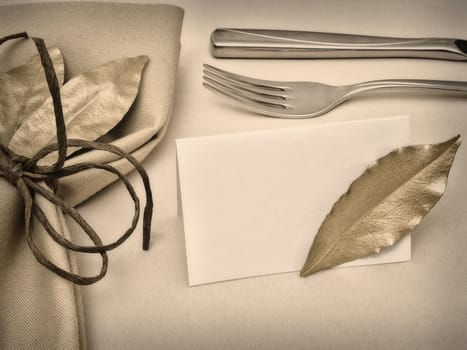 decorated table serving with golden bay leaves in serviette and cord near knife, fork and guest card at beige 