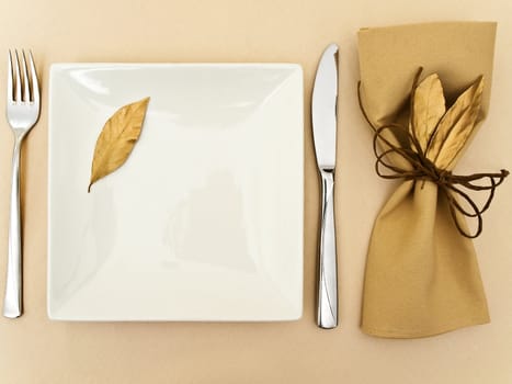 original table serving with golden bay leaves in serviette and cord near plate, knife and fork at beige 