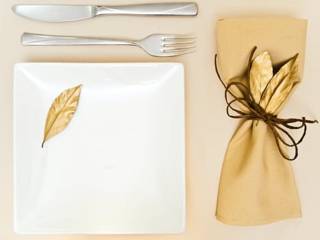 table serving with golden bay leaves in serviette and cord near plate, knife and fork at beige 