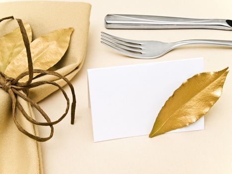 decorated table serving with golden bay leaves in serviette near knife, fork and guest card at beige 