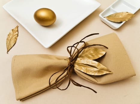 original table serving with golden bay leaves in serviette and cord near plate at beige  