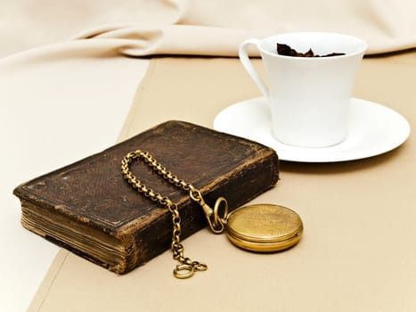 old pocket watch at the book near the cup of tea at beige 