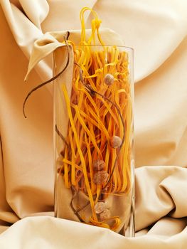 chili pasta decorated with nutmegs and cord in glass vase against beige textile