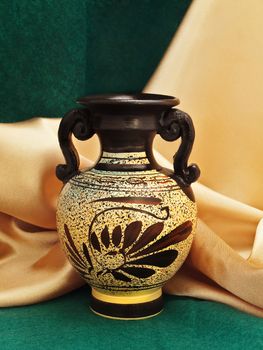Photo of antique vase against golden and green textile background