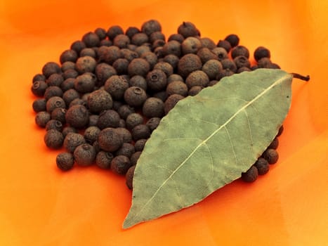 Photo of organic black pepper stack and single bay leaf at orange textile