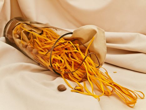 scattered chili pasta decorated with nutmegs and cord in glass vase at beige textile