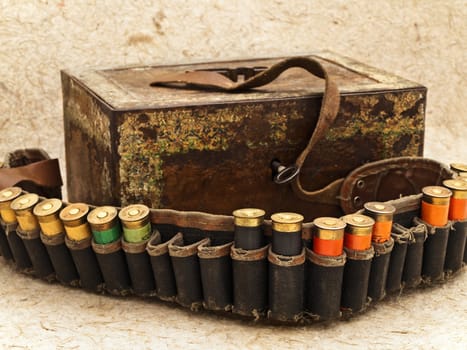 Photo of old ammunition belt with shells and vintage rusty chest against beige background