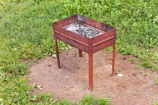 Brazier with charcoal and ashes after cooking on the green grass lawn