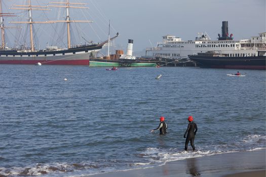 winter swimming and kayaking in San Fransisco Bay with historic ships of Hyde Street Pier and Alcatraz Island in background