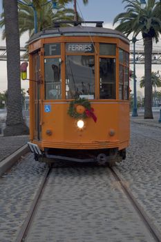 vintage orange streetcar on waterfront roadway (The Embarcadero) of San Francisco with palm trees and Bay Bridge in background