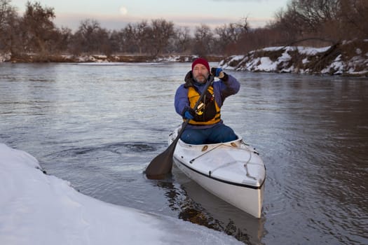 mature male paddling a decked expedition canoe on river in winter scenery (South Platte in eastern Colorado)