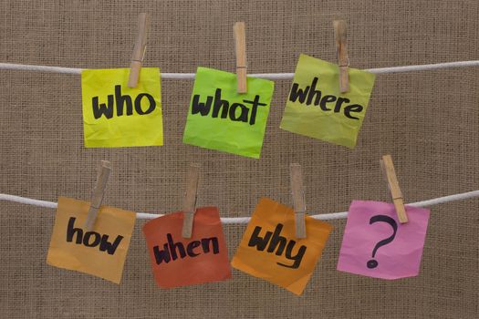who, what, where, when, why, how questions - uncertainty, brainstorming or decision making concept, colorful crumpled sticky notes hanging on clothesline against canvas background
