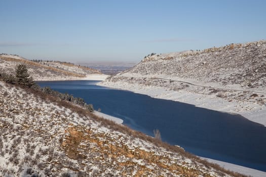 Horsetooth Reservoir in Colorado with highway and view of Fort Collins and plains over a dam, winter scenery with snow and still unfrozen water