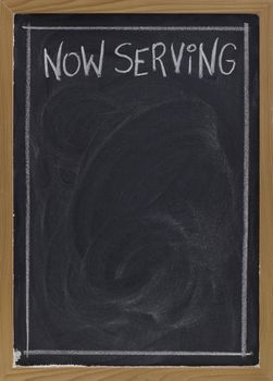 now serving - white chalk handwriting on blackboard with blank space below for a menu