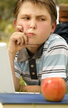 Boy working on a laptop with an expression of a problem/dilemma.  Could be used for study, schoolwork or homework.
