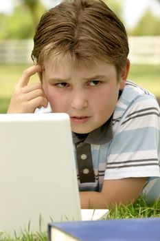 A puzzled looking boy working on computer outdoors.