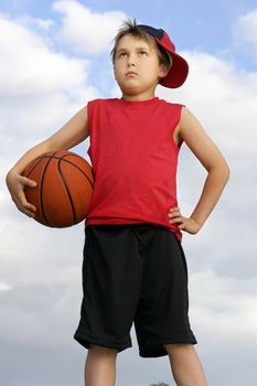 Boy in a red shirt and cap with a basketball under arm.