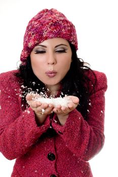 Winter woman wearing wool boucle jacket and woolen beanie blowing soft white flakes from palms of hands.