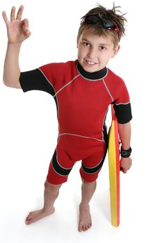 Boy with a surf gear shows the popular a-ok sign with his right hand while holding his board in the other.