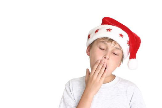 Tired boy wearing santa hat yawns
