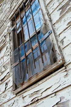 A boarded up window with broken blue panes of glass that has bars on it