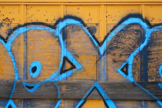 A tagger spraypainted some letters on the side wall of a yellow train boxcar