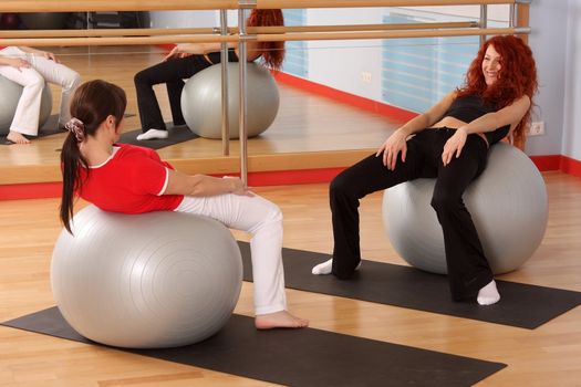 The pregnant woman with the instructor is engaged in gymnastics in a sports hall
