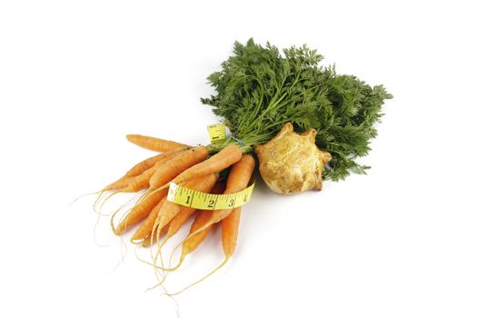 Contradiction between healthy food and junk food using bunch of carrots and pork pie with a tape measure on a reflective white background 