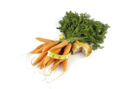 Contradiction between healthy food and junk food using bunch of carrots and pork pie with a tape measure on a reflective white background 